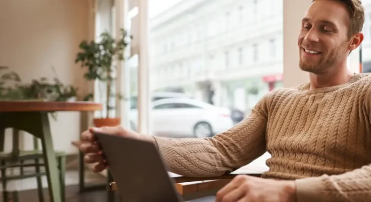 Retrato de um jovem profissional trabalhando sentado em um café com um laptop bebendo café e trabalhando online como freelancer usando o espaço de coworking para fazer seu trabalho. Retratando uma pessoa lendo dicas para anfitrião Foto: benzoix no Freepik